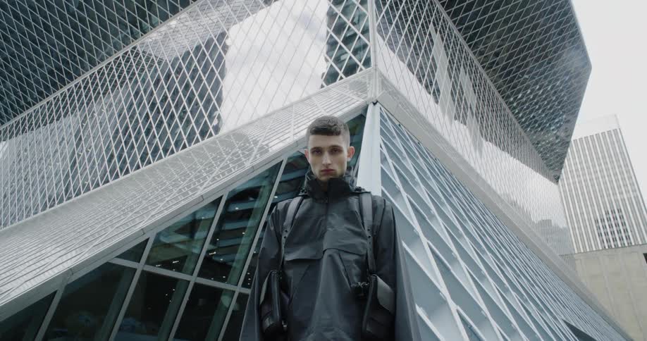The man looks down in front of the very tall building