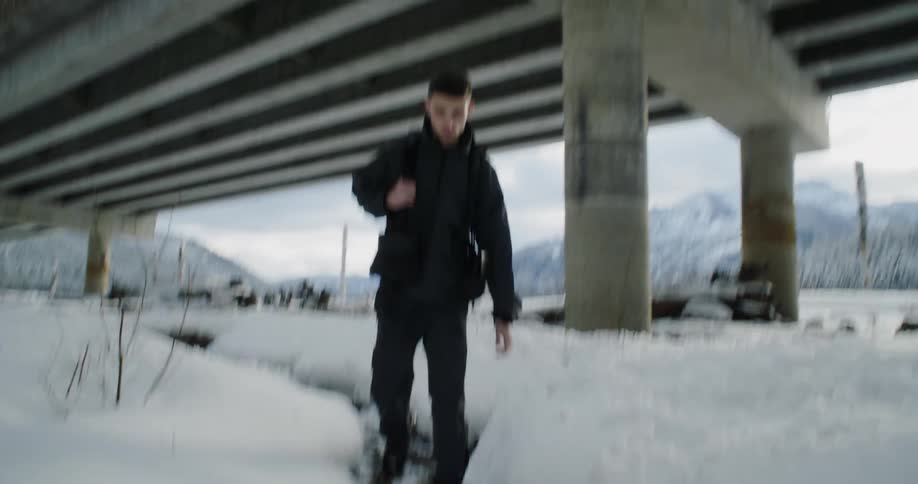 The man is hiking past the snow under the overpass