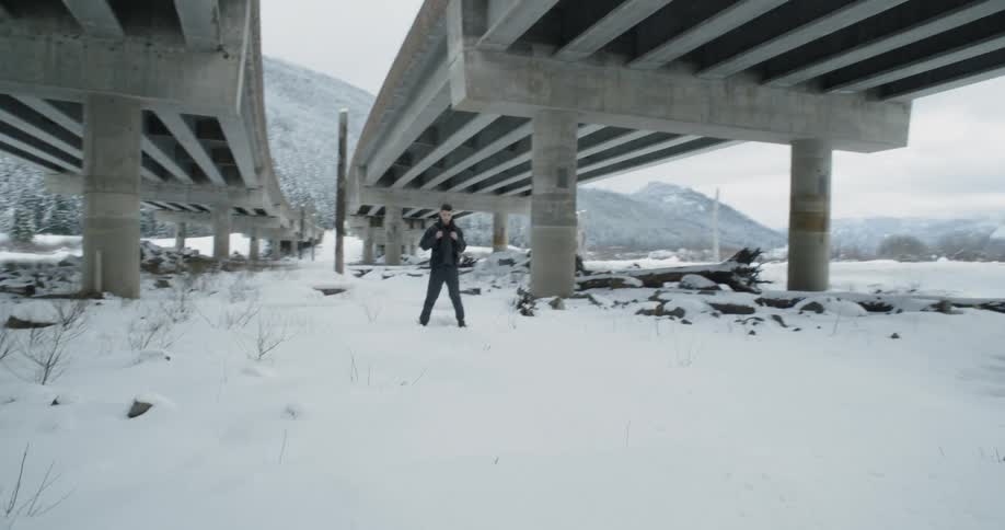 A man stands in snow beneath overpasses