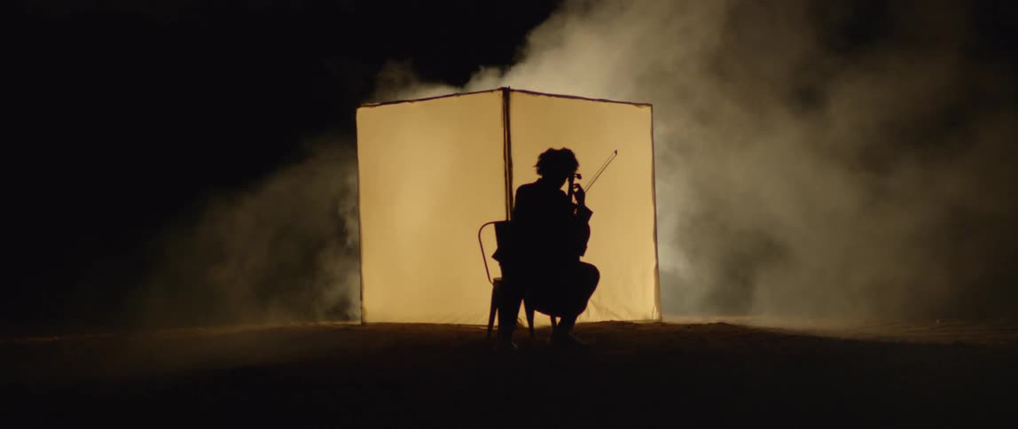 The silhouette of a person playing a string instrument with a bow