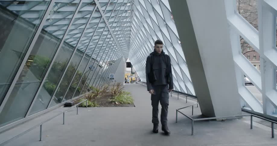 The man walks past the moving vehicles by the building