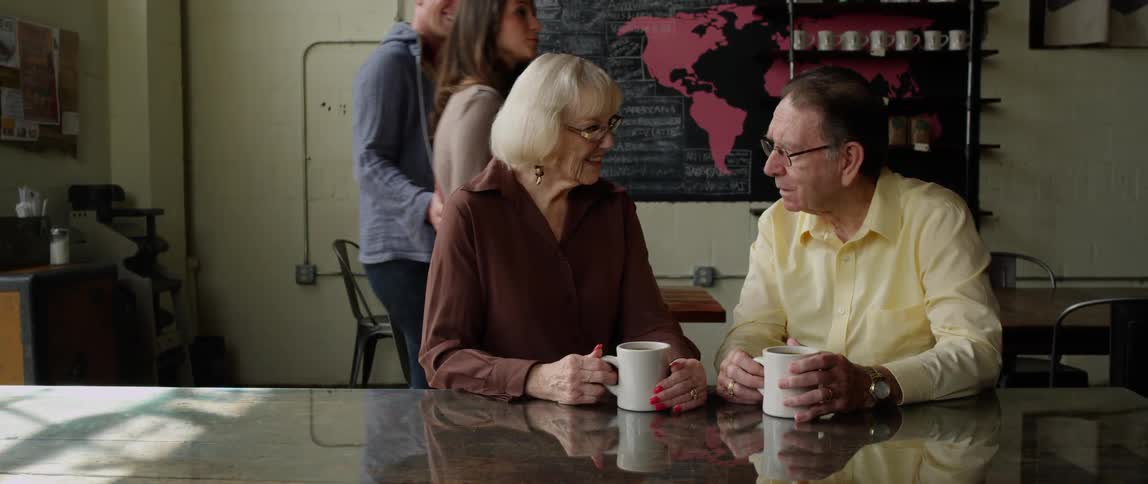 A man and woman have coffee in a shop as two others walk in to order