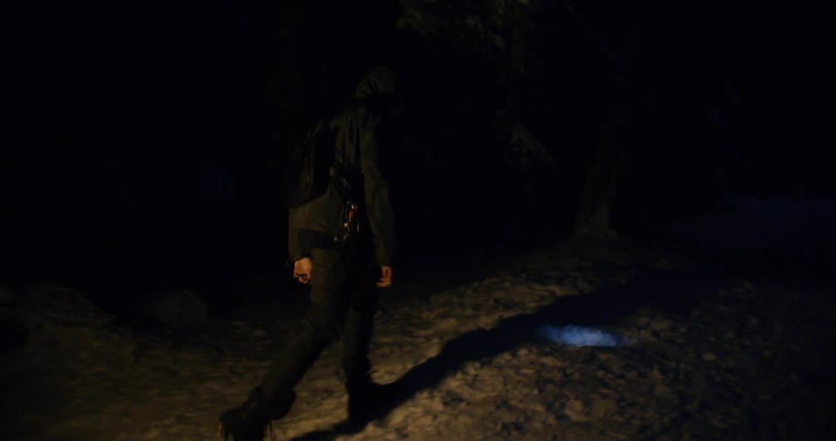 A man wearing a headlamp walks through the snow