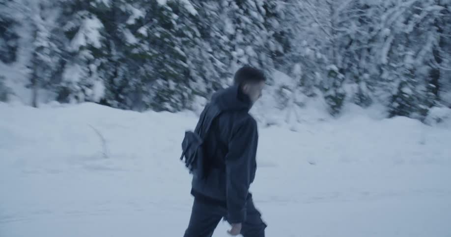 A man carrying a backpack walks through a snowy forest