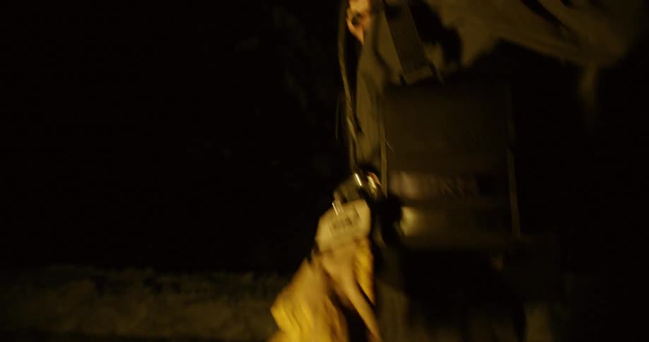 A man carrying a bag and wearing a headlamp walks on snow covered ground at night