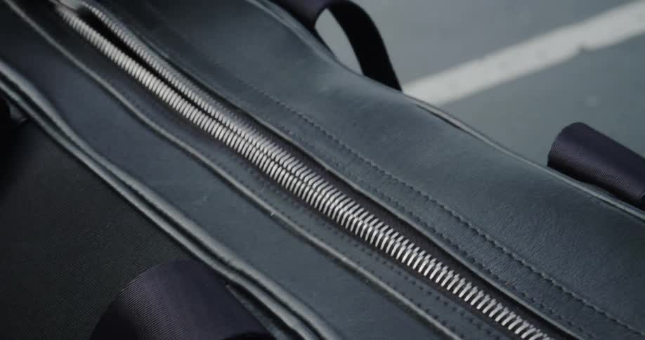The person unzips their luggage bag