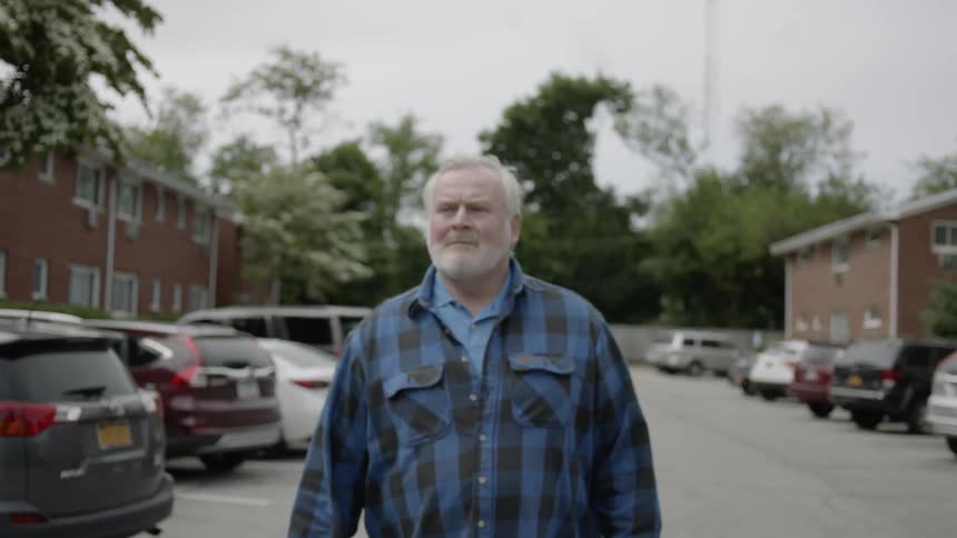 A man walks through an apartment complex parking lot on a cloudy day