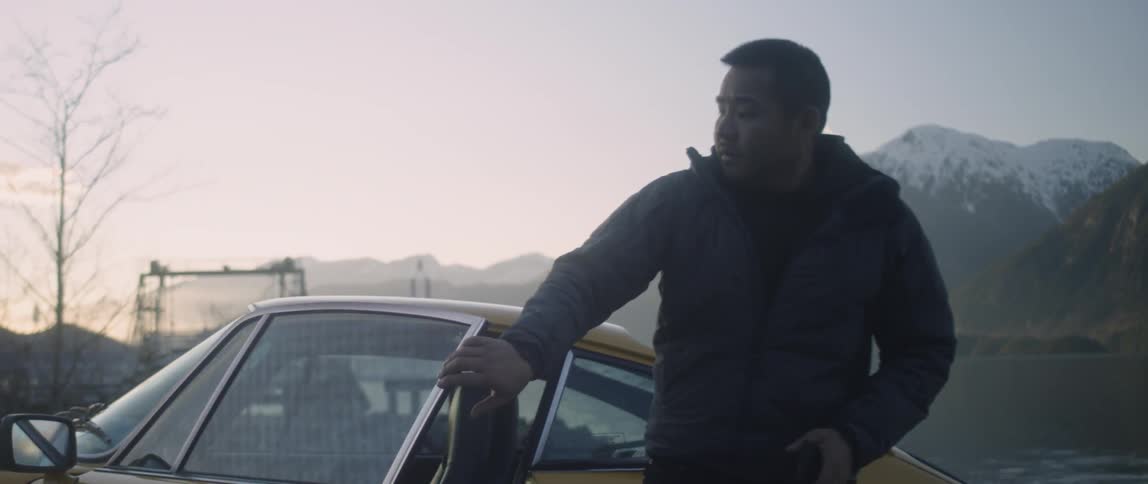 A man climbs out of a car parked in mountains at sunset