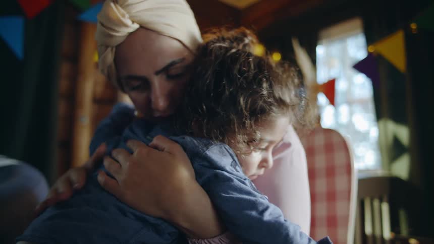 A woman sits on the floor hugging and rocking a little girl as she rubs her back