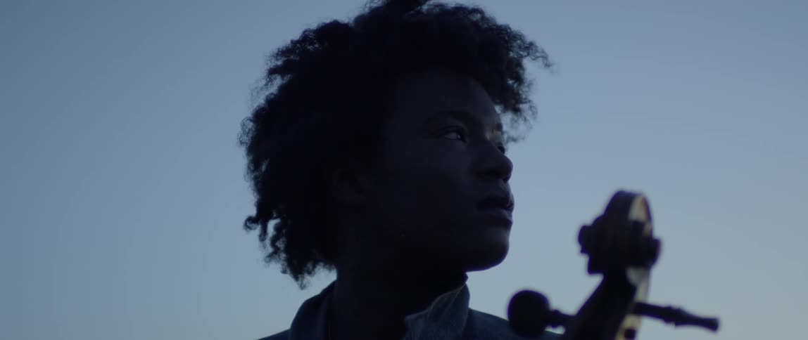 A woman plays a cello outside at dusk