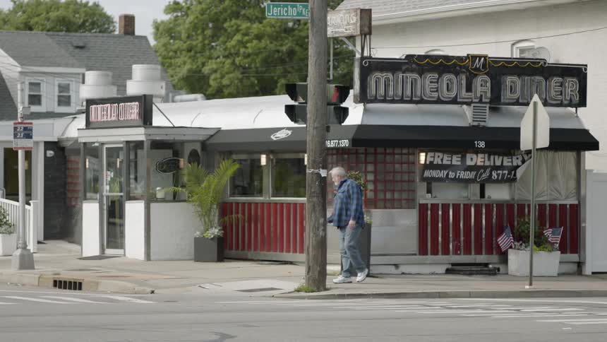 A man walks by a store on the corner as cars drive by