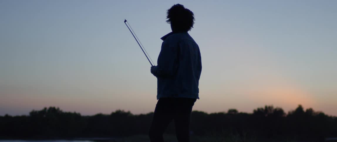 A cellist carries a bow outside at dusk