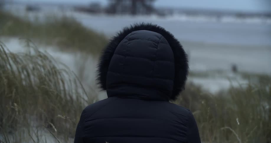 Woman wearing a coat stands on the beach