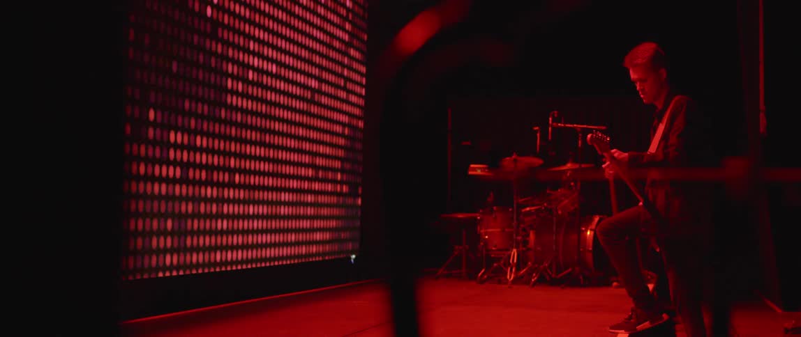 Man plays guitar on stage illuminated by red light