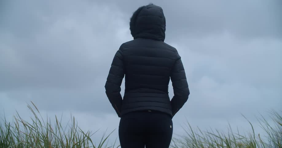A woman in a coat stands outside on a windy day