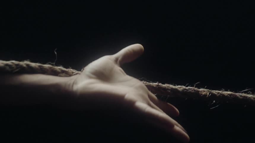 A man holds his arm outstretched as a rope moves along it in the dark