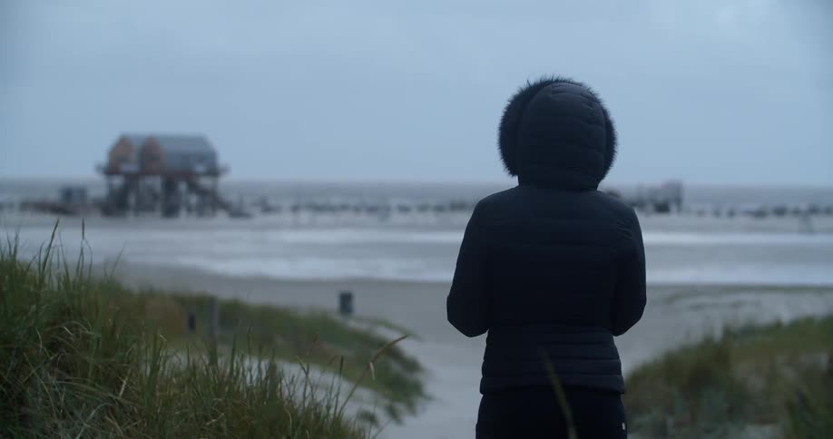 Woman wearing a coat stands on the beach