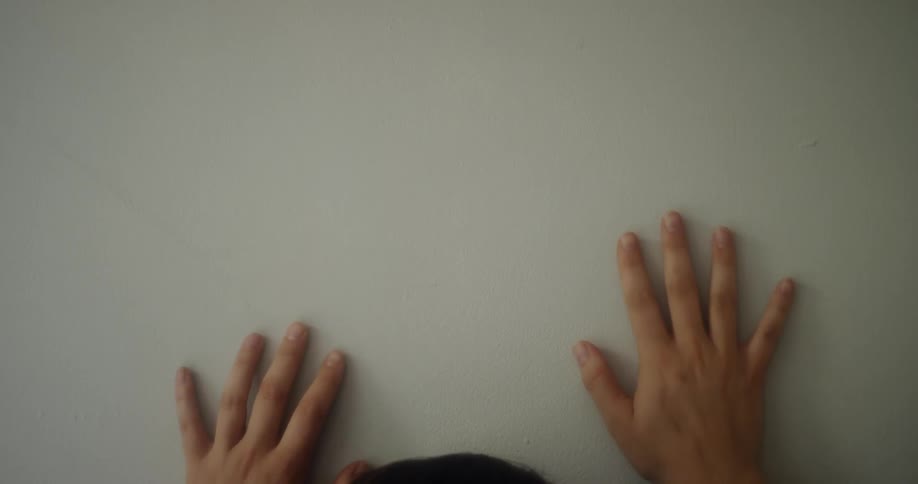 Two hands press against a white wall