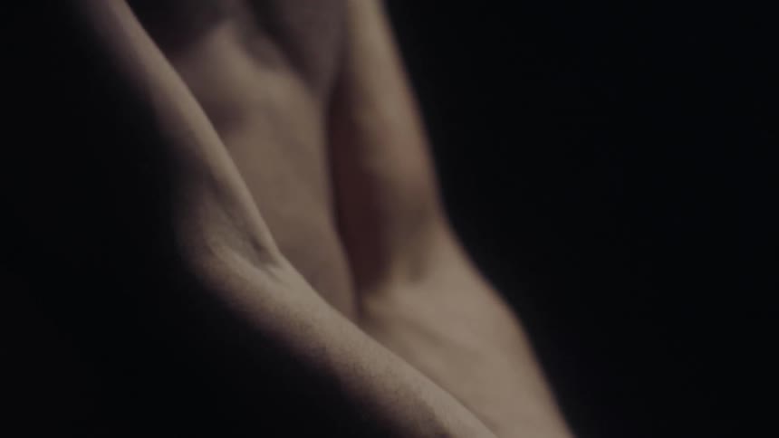 A shirtless man grabs his wrist and flexes his fingers