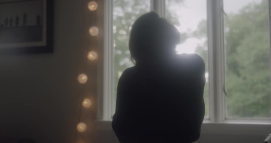 A woman rubs her neck and stretches near a window