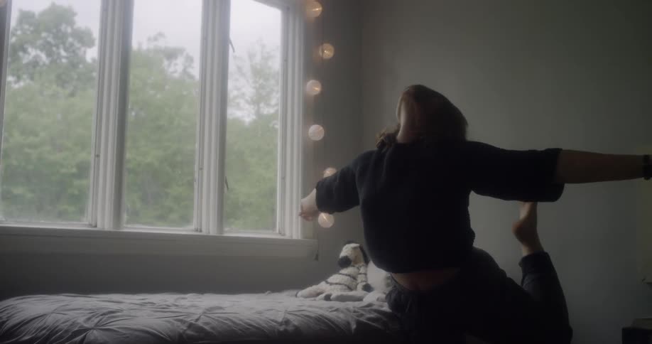 Woman balances on one leg in her bedroom