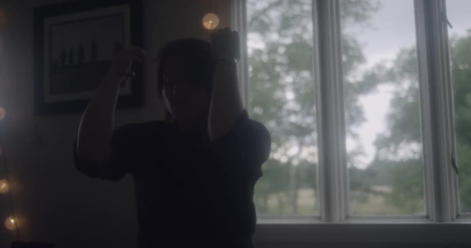A woman stands by a window and touches her hair before looking at her hands