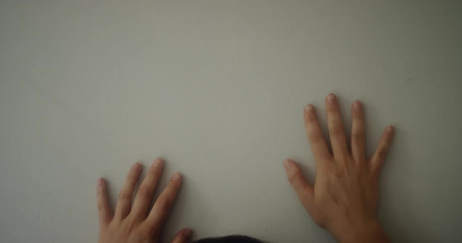 A person runs their hands up a white wall