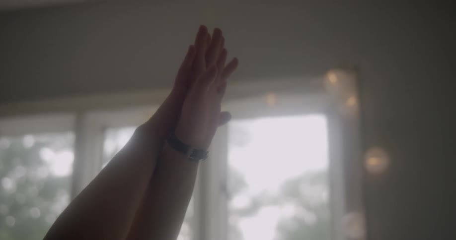 Person raises their arms in the air by a window