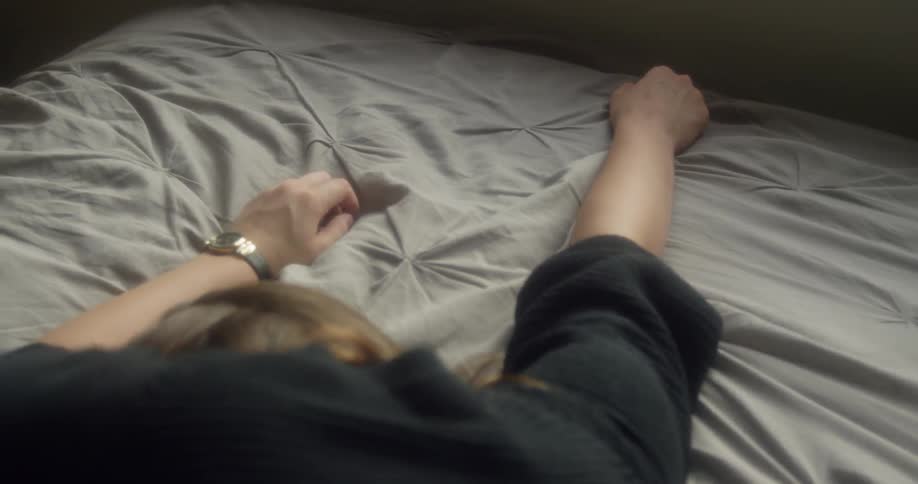 A woman lies face down on a bed and stretches out her arms