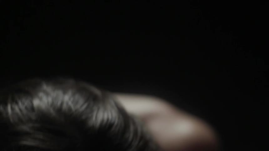 A shirtless man touches his hair while hunched over