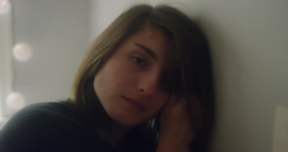 A sad woman leans against a wall