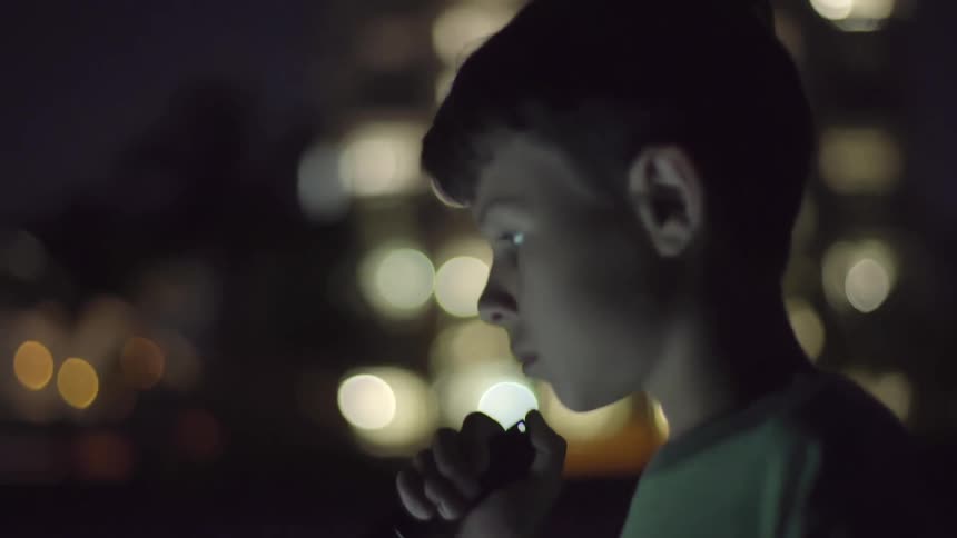 Young boy with a flashlight walking at night on a city street