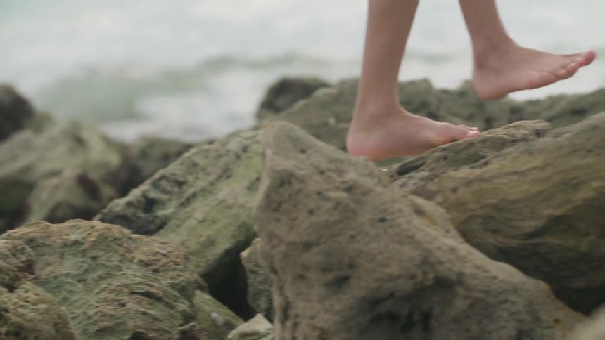 A boy balances on rocks at the beach