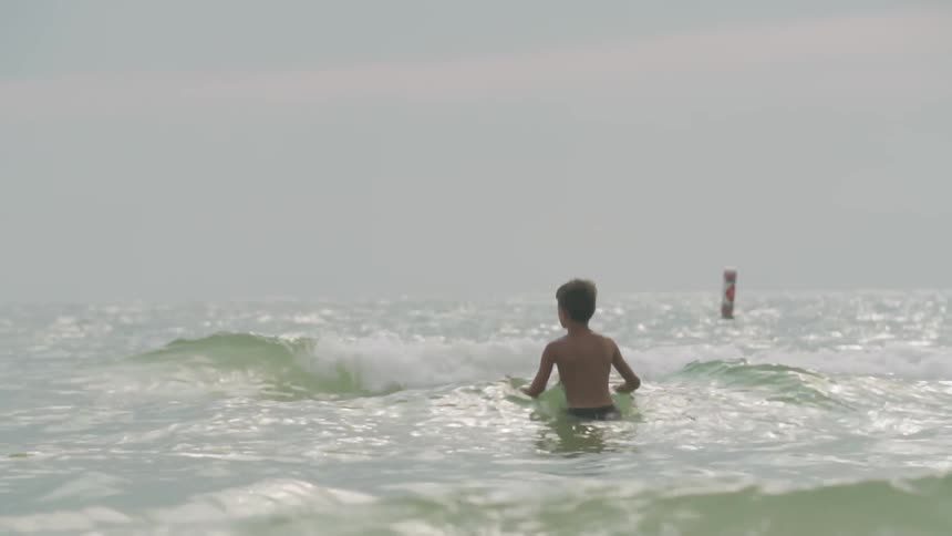A boy stands waist high in a ocean on a cloudy day
