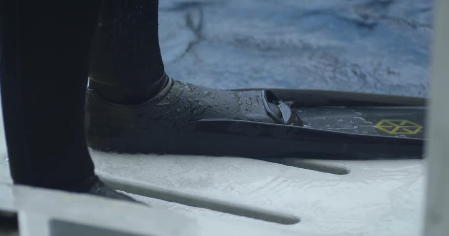 The person stands on the side of the boat wearing flippers