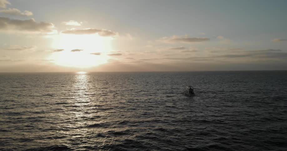 A boat travels on the ocean at sunset on a cloudy evening