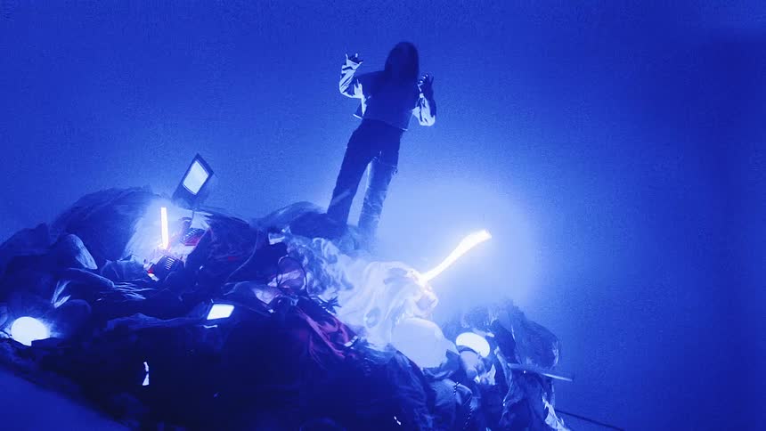 A woman stands on a mound of clothing and flashing lights