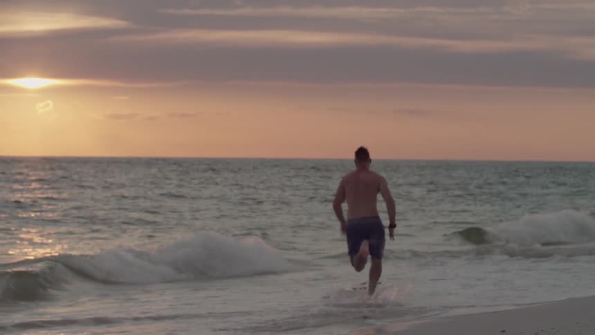A man running towards the ocean to ride a surfboard at dusk