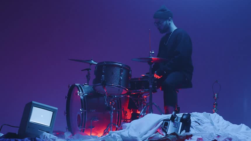 A drummer plays on top of a pile of random objects