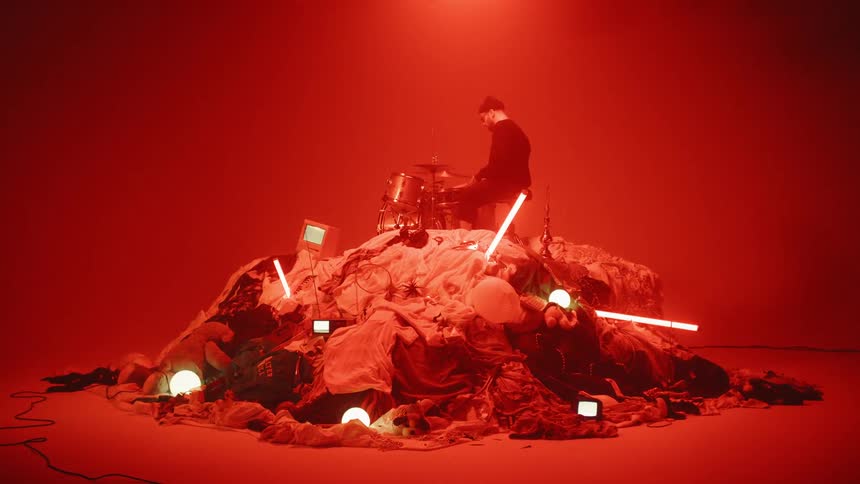 A drummer plays on top of a pile of random objects