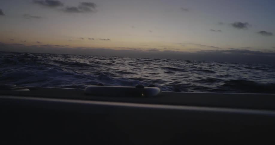 A boat travels on the ocean at sunset with some clouds in the sky