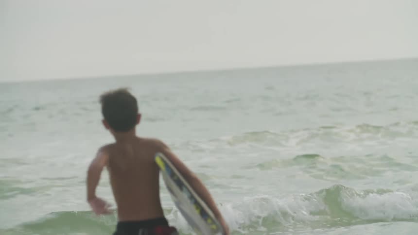 A boy runs towards the ocean with a boogie board