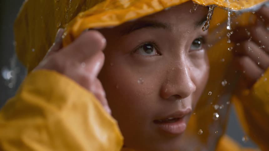 The woman looks up at the rain lifting her hood
