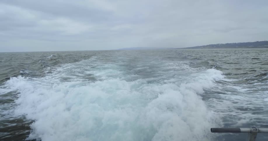 The water behind a boat as it travels on the ocean on a cloudy afternoon