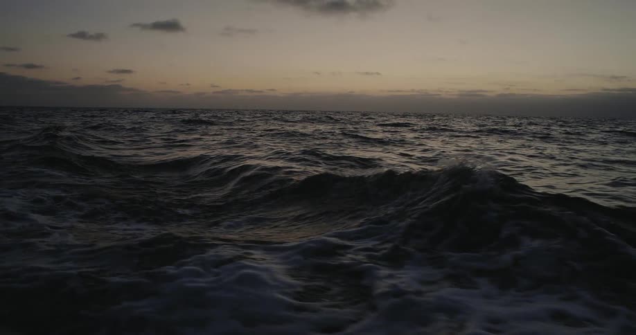 Waves and choppy water in the ocean at sunset with clouds in the sky