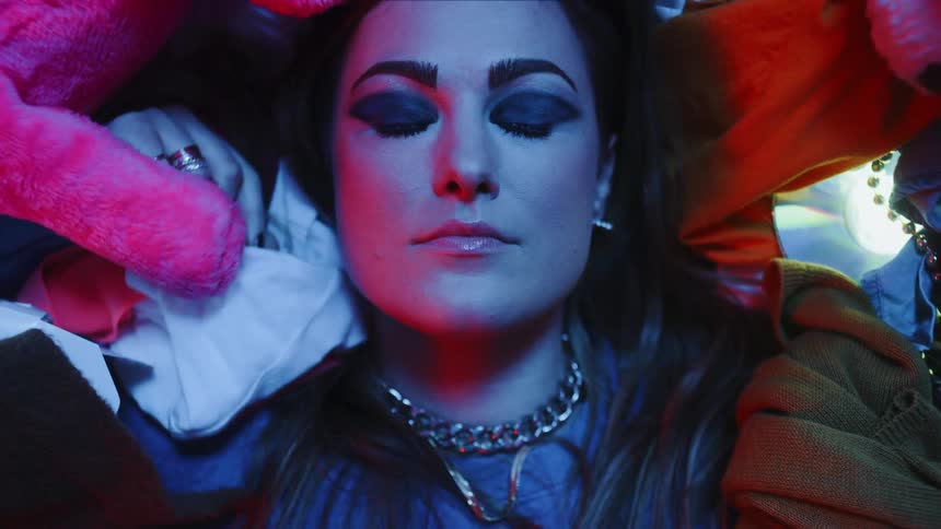 A woman lying on clothes and stuffed animals opens her eyes