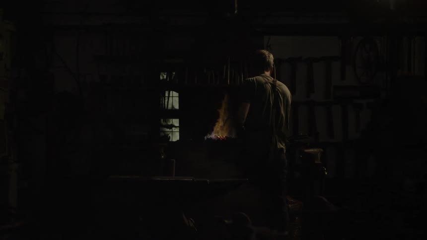 A blacksmith works next to a fire