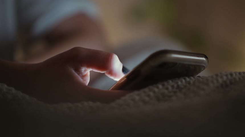 Person lays in bed scrolling on a phone