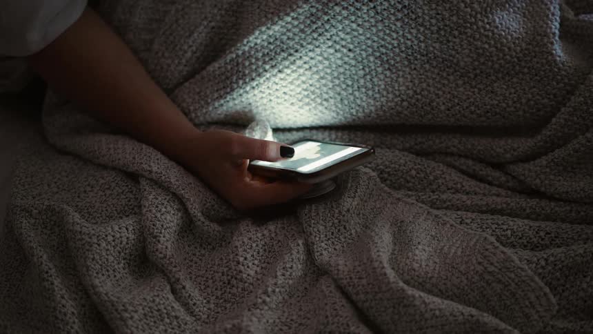 The person is using their phone in bed