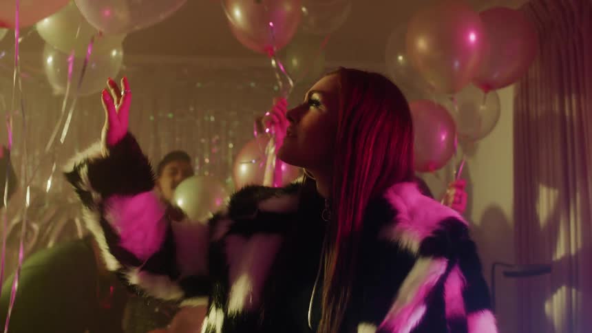 Woman in a checkered coat reaches towards the floating balloons